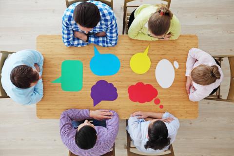 Overhead view of people sitting at a table with empty thought bubbles.
